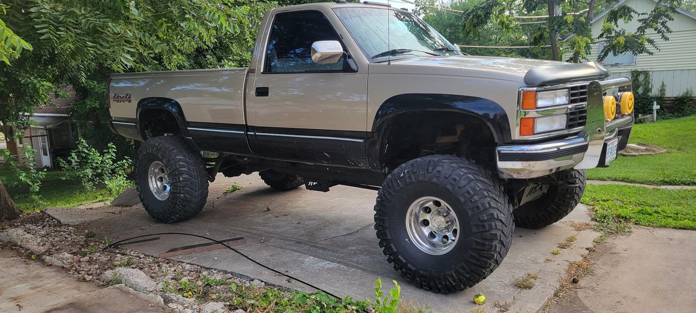 A lifted tan and black Chevrolet pickup on off-road tires